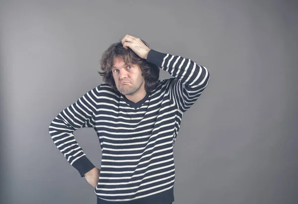 Puzzled guy with messy hair, frowning and looking unsatisfied scratching head, thinking deeply about something on grey wall background. Human facial expression, emotion, feeling, sign body language.