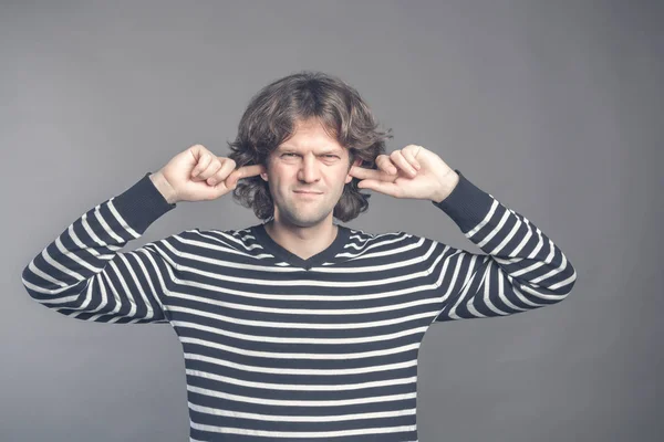 El hombre disgustado tapando las orejas con los dedos no quiere escuchar nada aislado en el fondo de la pared gris. Joven macho guapo cubriendo oídos ignorando el ruido. Sufriendo de un fuerte sonido. Lenguaje corporal — Foto de Stock