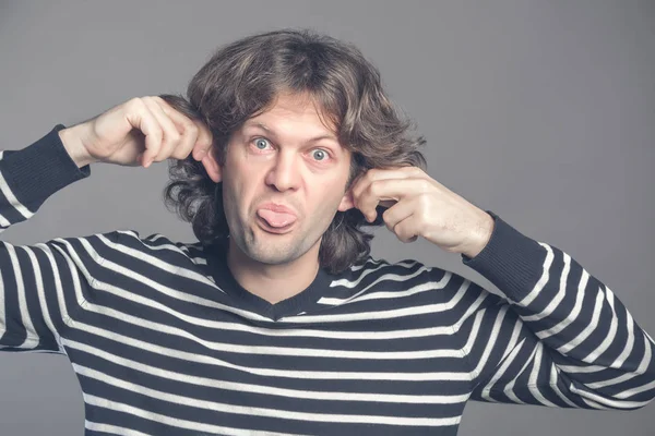 Primer plano del hombre haciendo cara de mono tonto aislado sobre fondo gris. El tipo mueca al mono. Divertido macho sosteniendo sus orejas y muestra la lengua parece mono, fingiendo chimpancé, entreteniendo a los niños — Foto de Stock