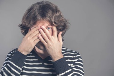 Korkmuş adam kapakları yüz iki elinizle, parmaklar, korkuyla, peeks aracılığıyla görünüyor fotoğrafı siyah kıvırcık saçlı, gri arka plan, metniniz için boş alan üzerinde izole rahat jartiyer giymiş vardır.