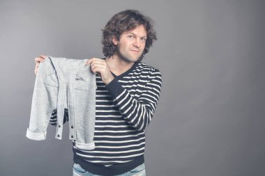 Genç beyaz erkek yeni şık bebek giysileri hakkında elinde tutan ve gri gösteren oğlu övünme için kamera pantolon. Kameraya bakarak ve yeni elbiseler üzerinde palavra gülümseyen adam. Kopya alanı.