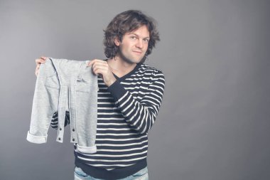 Young caucasian male boasting about new stylish baby clothes for his son holding in hands and demonstrating grey pants to camera. Man smiling looking at camera and bragging new clothes on. Copy space. clipart