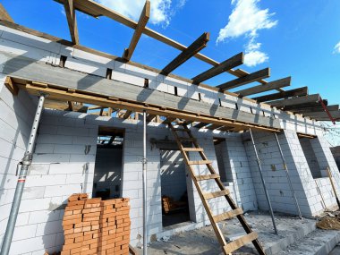 A building under construction, with a blue sky in the background. The image shows the framing of a house with support structures. grainy texture