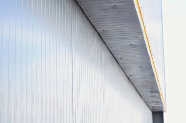 Bükülmüş metal kaplamalı ve açılı çatısı olan bir binanın yan tarafındaki soyut bir mimari çekim..