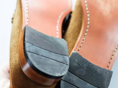 İki kahverengi süet ayakkabının alt kısmının detaylı görüntüsü, desenli lastik tabanlar ve dikişler. Ayakkabılar iyi yapılmış ve şık görünüyor..