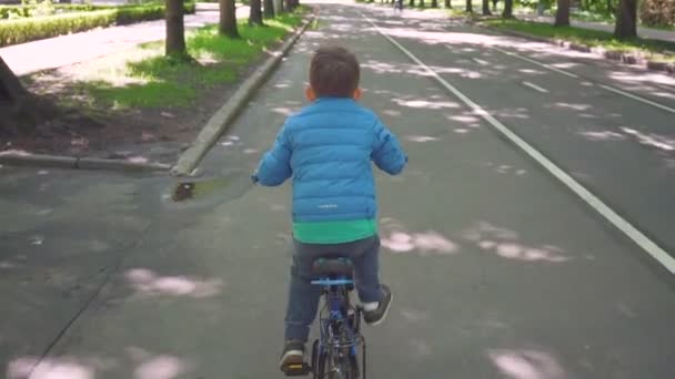 Маленький хлопчик верхи на синьому велосипеді в міському парку — стокове відео