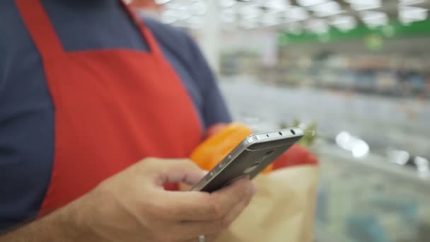 Repartidor con bolsa de papel de supermercado tomando un pedido utilizando un teléfono inteligente — Vídeos de Stock