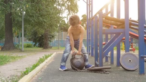 Menino levantando kettlebell pesado no chão de esportes ao ar livre — Vídeo de Stock