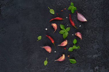 Yemek pişirmek için malzemeler. Koyu arka plan üzerine sarımsak, fesleğen ve kırmızı biber üstten görünüm.