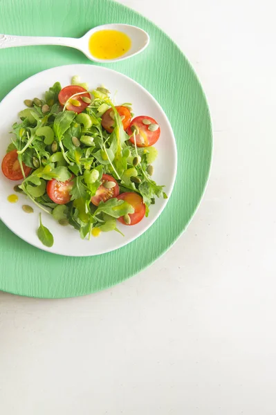 Vegetariánský salát s rukolou, cherry rajčátky a slunečnicová semínka na bílé keramické desky, pohled shora, kopírovat prostor — Stock fotografie