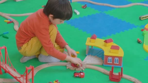 Niño jugando con el ferrocarril de madera en el suelo — Vídeo de stock