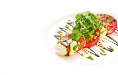 Beyaz plaka mozarella peyniri, domates, roka ve pesto soslu salata.