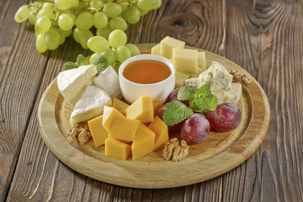 Cheese plate served with grape, nuts and honey on wooden background