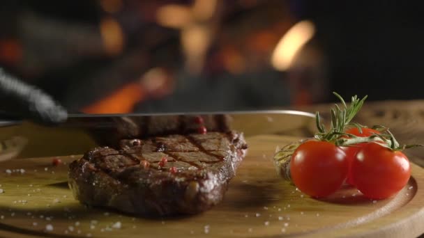 Fleischsteak auf Holzbrett über Feuerhintergrund schneiden. — Stockvideo