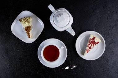 İki parçası cheesecake, fincan çay ve siyah arka plan üzerine çaydanlık. Üstten Görünüm, düz lay