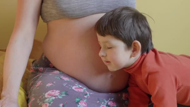 Мальчик слушает маму беременной животик — стоковое видео