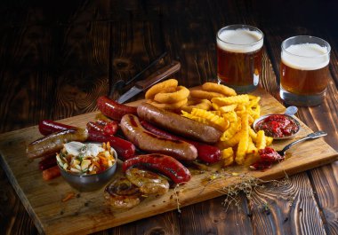 Aperatifler ızgara sosis, kızarmış patates, soğan halkaları ve iki bardak bira ahşap Pano rustik ahşap tablo.