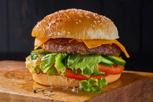 Delicioso hambúrguer com carne, tomate, salada e molho a bordo em fundo de madeira — Fotografia de Stock