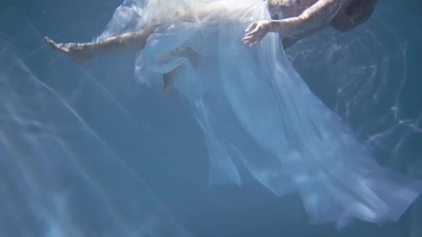 Молодая блондинка в винтажном белом платье плавает под водой — стоковое видео