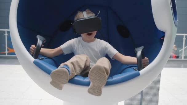 Menino desfrutando de atração de realidade virtual usando fone de ouvido VR em uma cadeira interativa em movimento — Vídeo de Stock