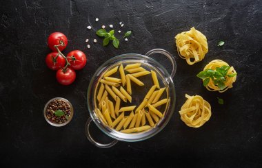 Siyah kayrak arka planda fesleğen ve domates ile çiğ makarna farklı türleri. Üstte görüntü.