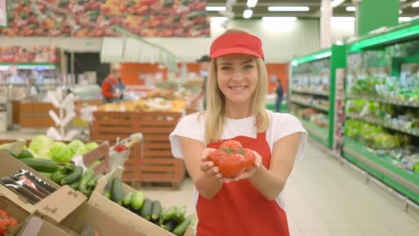 Молодая продавщица улыбается и держит свежие помидоры в супермаркете . — стоковое видео