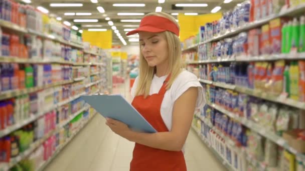 漂亮的五金店工人拿着剪贴板，站在超市的货架上 — 图库视频影像