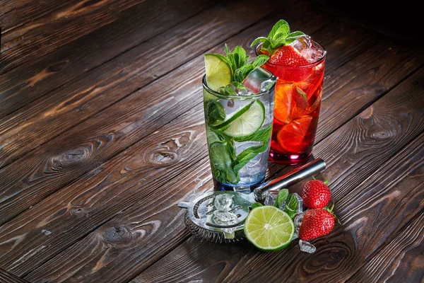 Mojito drinkar med lime, jordgubb och mynta i glas med isbitar på trä bakgrund — Stockfoto