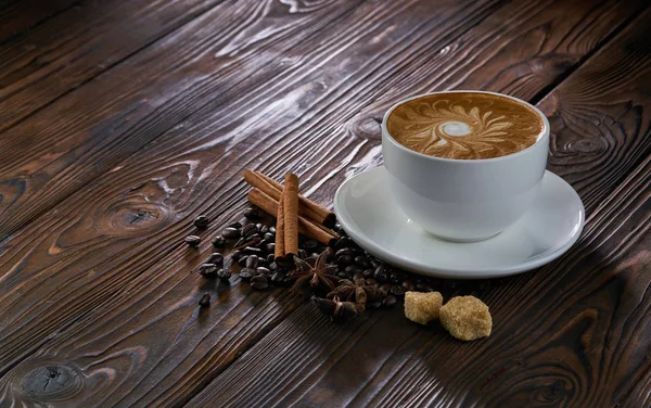 Een kopje cappuccino met koffiebonen, kaneel en bruine suiker op houten tafel — Stockfoto