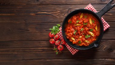 Makarna penne domates sosu ve fesleğen demir döküm tavada. Ahşap masa, fotokopi alanı ile üst görünüm