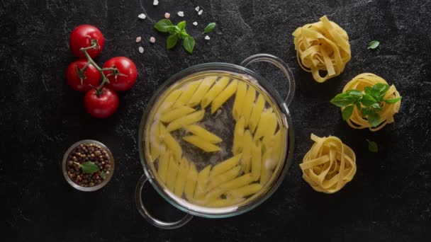 Laço de cinematografia. Cozinhar penne de macarrão em uma panela de vidro com água fervente — Vídeo de Stock