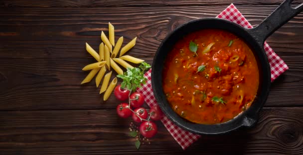 Kinotag. Nudeln Penne mit Tomatensauce und Basilikum auf Eisenguss Pfanne kochen. Holztisch, Ansicht von oben — Stockvideo