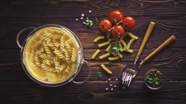 Cinemagraph - cottura pasta fusilli in acqua bollente in pentola di vetro su tavola di legno — Video Stock