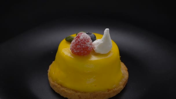 Десерт мусу, покритий жовтою глазур'ю, що обертається на чорній тарілці — стокове відео