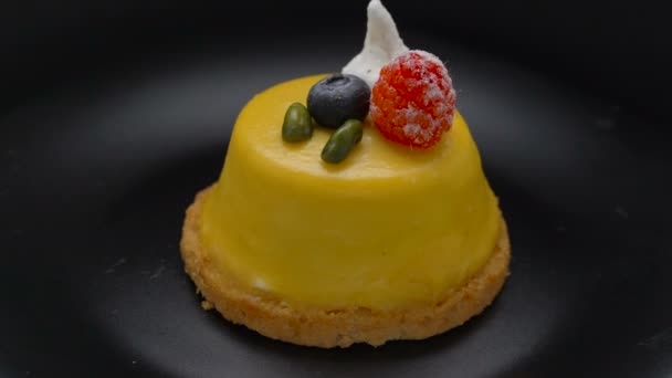 Mango mousse cake covered with yellow glaze rotating on black plate — Stock Video
