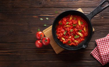 Makarna penne domates sosu ve fesleğen demir döküm tavada. Ahşap masa, fotokopi alanı ile üst görünüm