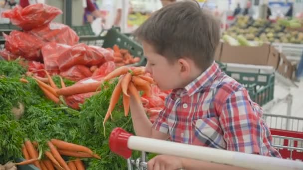 Aranyos kis fiú választotta friss szerves sárgarépa a szupermarketben. Egészséges életmód fiatal családnak gyerekekkel — Stock videók