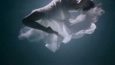 Suyun altındaki genç kadın, beyaz bir elbise giyiyor..