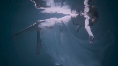 Beyaz zarif elbise ile su altında yüzen güzel kadın