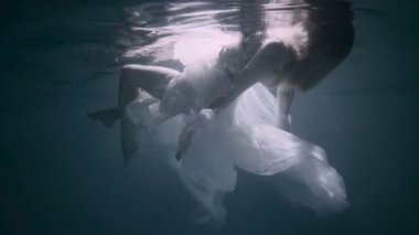 Suyun altındaki genç kadın, beyaz bir elbise giyiyor..