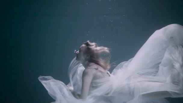 Krásná žena plavala pod vodou v bílých elegantních šatech