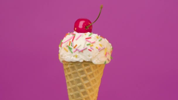Ванильное мороженое в конусе с брызгами и вишней на красочном фоне — стоковое видео