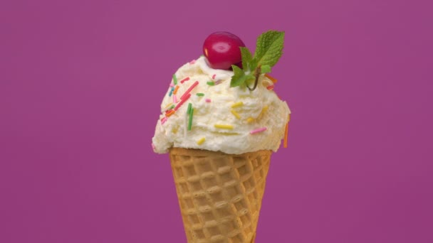 Cuchara de helado de vainilla en cono de gofre con hoja de menta verde y cereza fresca decorada con espolvoreos de colores — Vídeo de stock