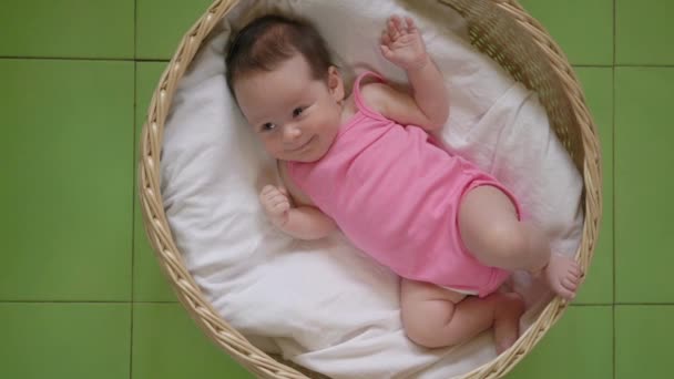 Красивая новорожденная девушка в розовом купальнике в корзине на зеленом фоне, вид сверху — стоковое видео