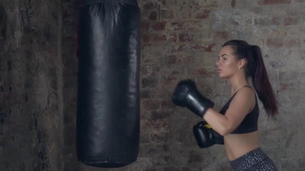 Side view of young girl in black boxing gloves training technique with punching bag — Stock Video