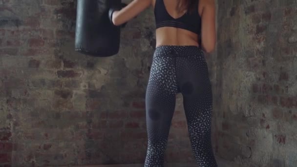 Вид ззаду сексуальна дівчина в чорному спортивному одязі тренування з мішком для ударів — стокове відео