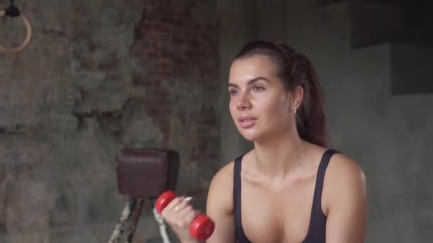 Meisje in zwarte Sportswear workout met dumbbells zittend op Swiss-ball op de achtergrond van een bakstenen muur — Stockvideo