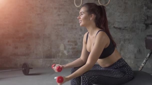 Young beautiful sexy girl on fitness ball at gym with red dumbbells, sport and healthy lifestyle concept — Stock Video