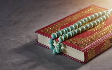 Gri arka planda tespih boncuklu İslami kitap Kuran