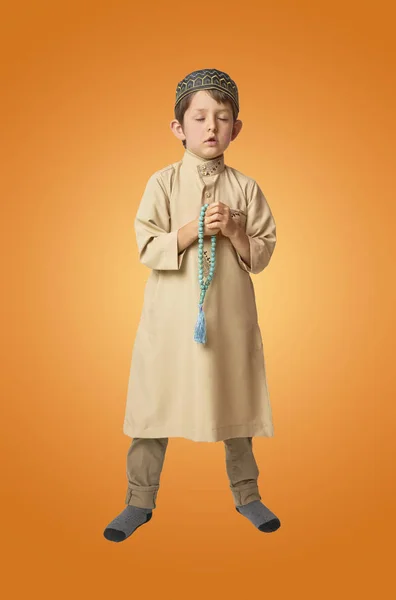 Piccolo ragazzo musulmano che prega e tiene perline di preghiera su sfondo colorato — Foto Stock